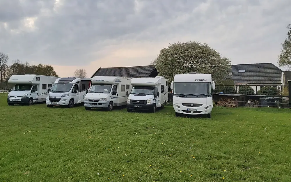 Fünf weiße Wohnmobile, die nebeneinander auf einer Wiese geparkt sind, mit Häusern, Bäumen und einem bewölkten Himmel im Hintergrund - die perfekte Inspiration, wenn Sie Ihr Wohnmobil verkaufen oder ein gebrauchtes Wohnmobil verkaufen möchten.