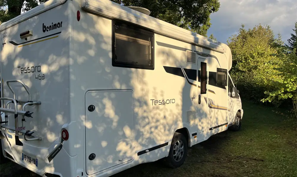 Weißes Benimar Tessoro 463 Wohnmobil geparkt auf Gras, umgeben von grünen Bäumen im Tageslicht - ideal für wohnmobil ankauf oder diejenigen, die gebrauchtes wohnmobile verkaufen in einer schönen Umgebung.