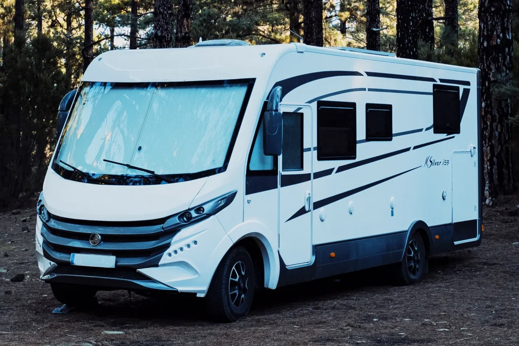 Ein weißes Wohnmobil mit schwarzen Akzenten parkt in einem Waldgebiet zwischen hohen Bäumen - die perfekte Inspiration, wenn Sie Ihr Wohnmobil verkaufen möchten.